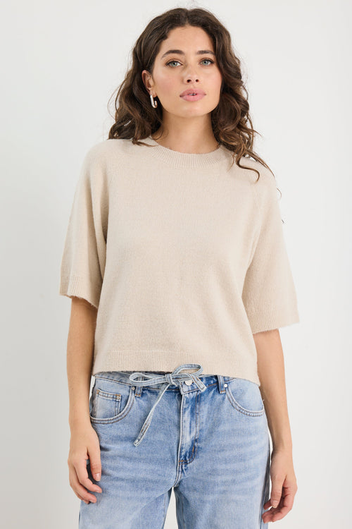 Woman wearing a beige sweater and blue jeans against a white background