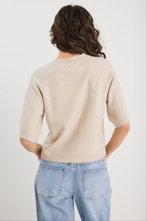 Person wearing a beige sweater and blue jeans on a white background