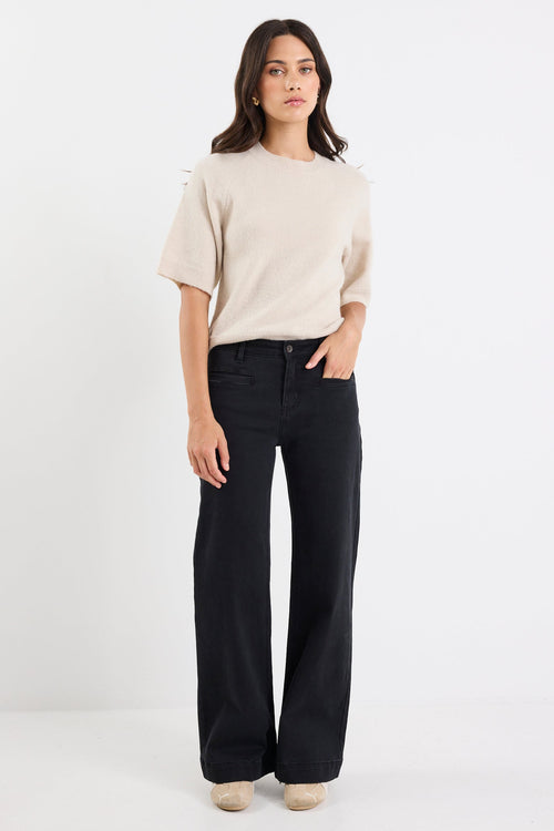 Woman wearing a beige sweater and black jeans on a white background