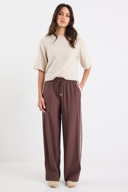 Woman wearing a beige top and brown pants on a white background