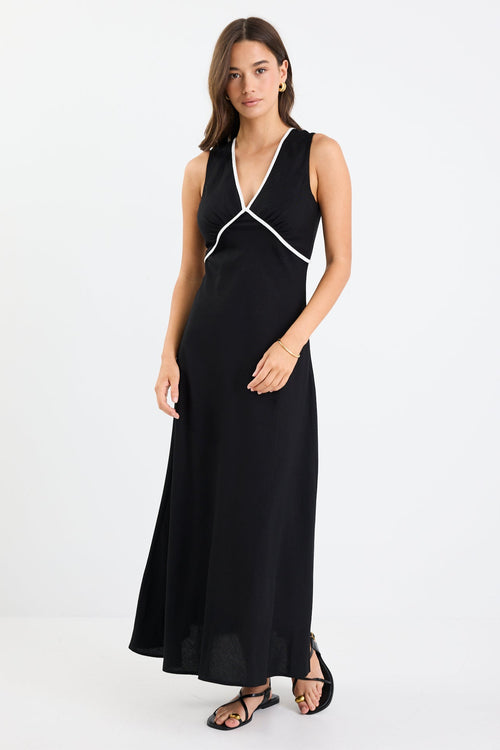 Woman wearing a black sleeveless maxi dress with a V-neckline, white contrast binding detail, bias cut, and softly flared hem.
