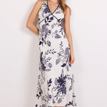 A woman modeling a sleeveless midi dress with a navy blue floral print on a white background, standing against a plain white studio backdrop.