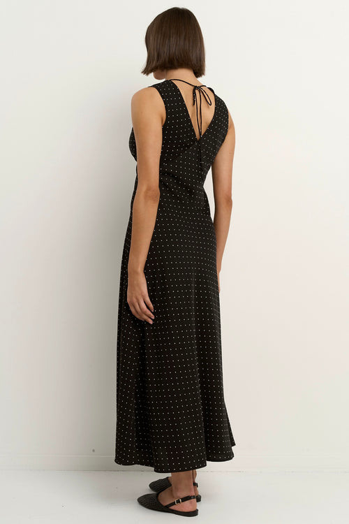 Woman wearing a sleeveless black midi dress with a V-neckline and small white polka dots, styled in a softly flowing silhouette.