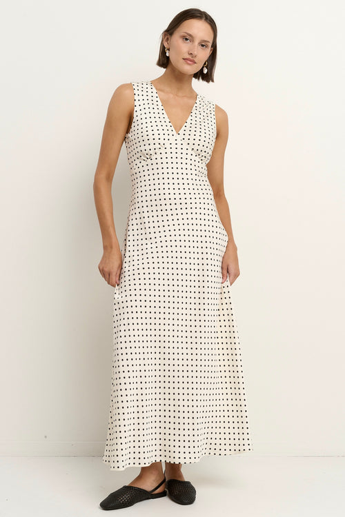Woman wearing a sleeveless white midi dress with a V-neckline and small black polka dots, styled in a softly flowing silhouette.