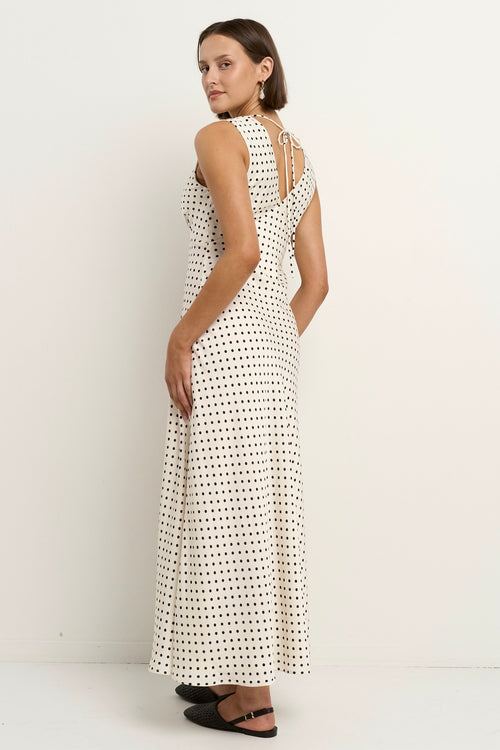 Woman wearing a sleeveless white midi dress with a V-neckline and small black polka dots, styled in a softly flowing silhouette.