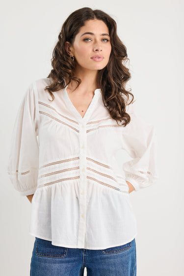 Woman wearing a white blouse with lace details and blue jeans on a white background