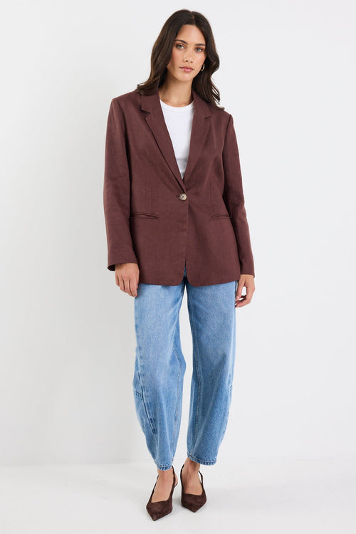 Woman wearing a brown blazer and blue jeans on a white background