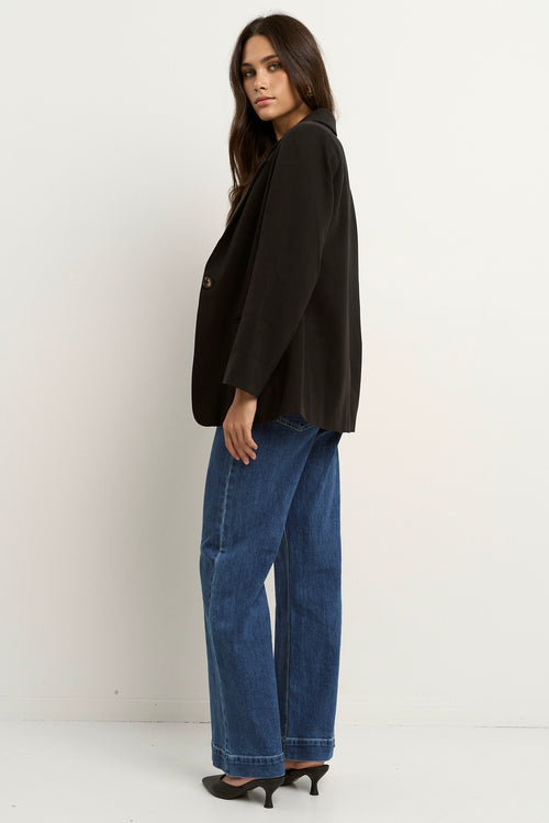 model wears a black blazer with blue jeans