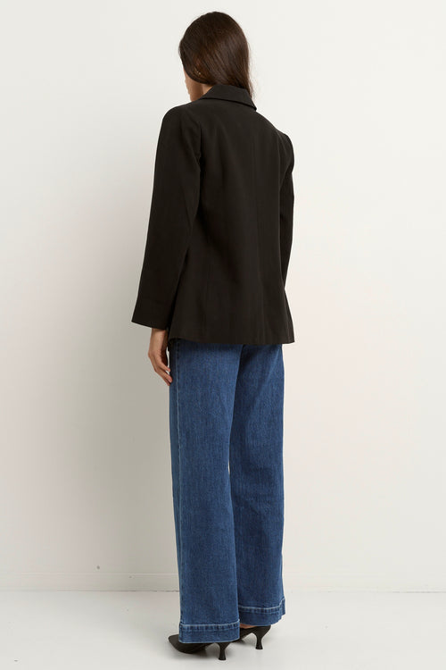 model wears a black blazer with blue jeans