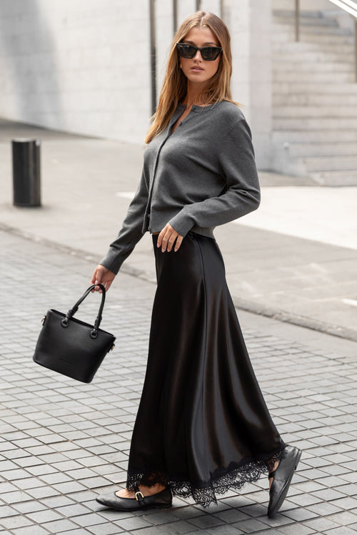 Woman in a gray sweater and black skirt walking on a sidewalk.