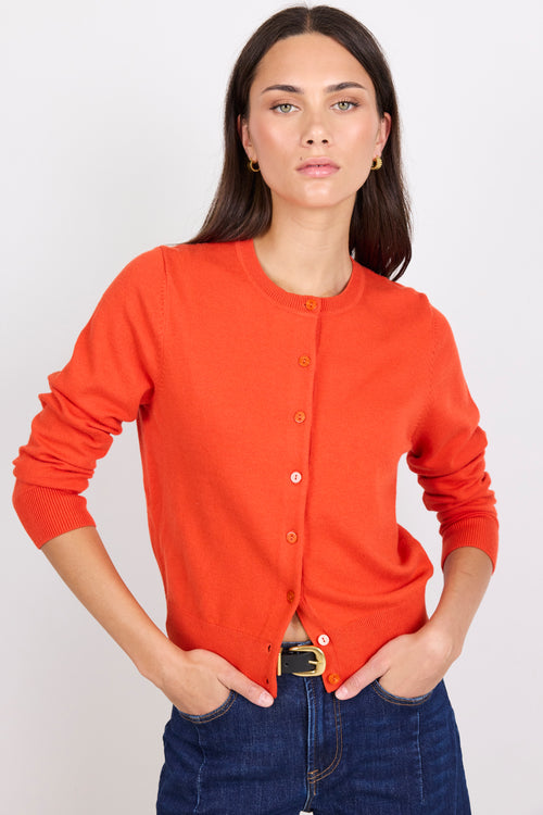Person wearing an orange cardigan and dark blue jeans on a white background