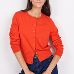 Person wearing an orange cardigan and dark blue jeans on a white background