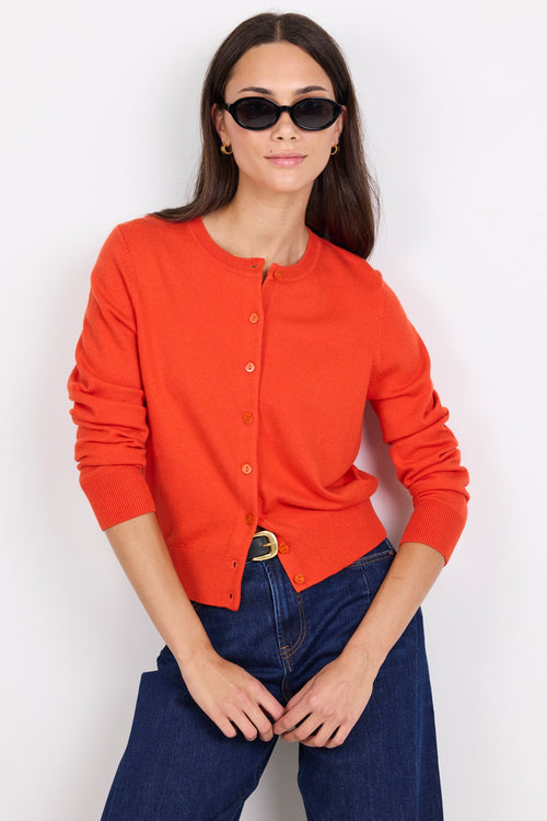 Person wearing an orange cardigan and dark blue jeans on a white background
