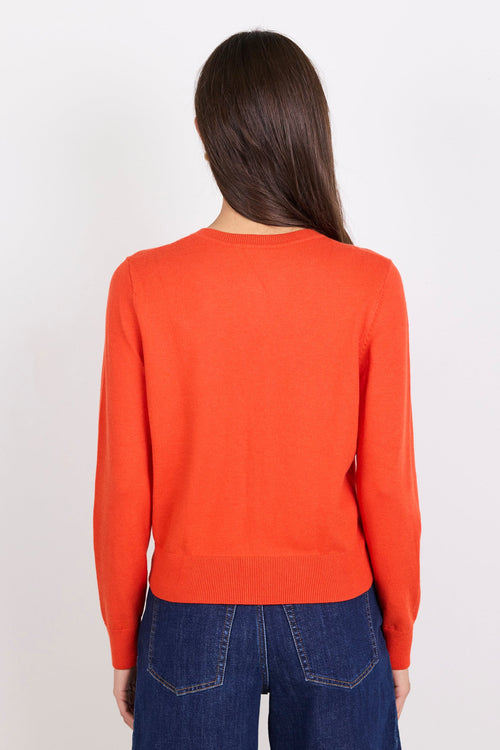 Person wearing an orange cardigan and dark blue jeans on a white background