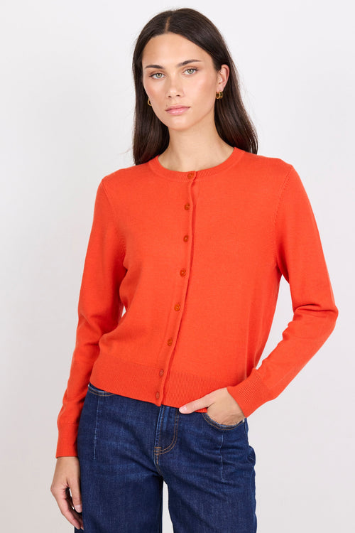 Woman wearing an orange cardigan and blue jeans on a white background