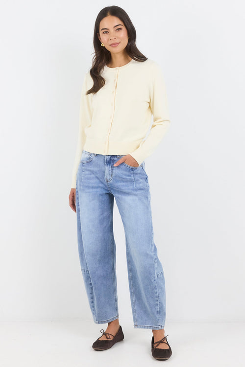 Woman wearing a light-colored top and blue jeans on a white background