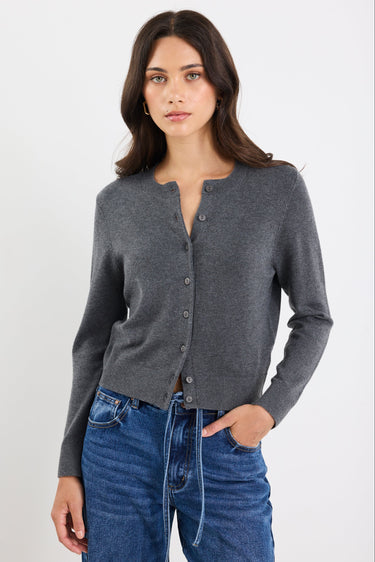 Woman wearing a gray cardigan and blue jeans against a white background