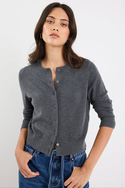 Woman wearing a gray cardigan over a black top with blue jeans on a white background