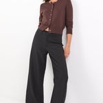 Woman wearing a brown cardigan and black pants against a white background