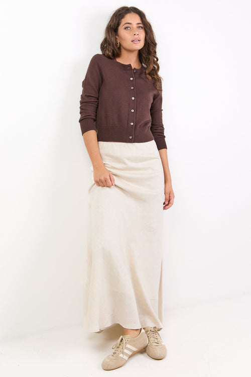 Woman wearing a brown cardigan, white skirt, and gold shoes on a white background