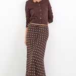 Woman wearing a brown button-up shirt and patterned skirt on a white background