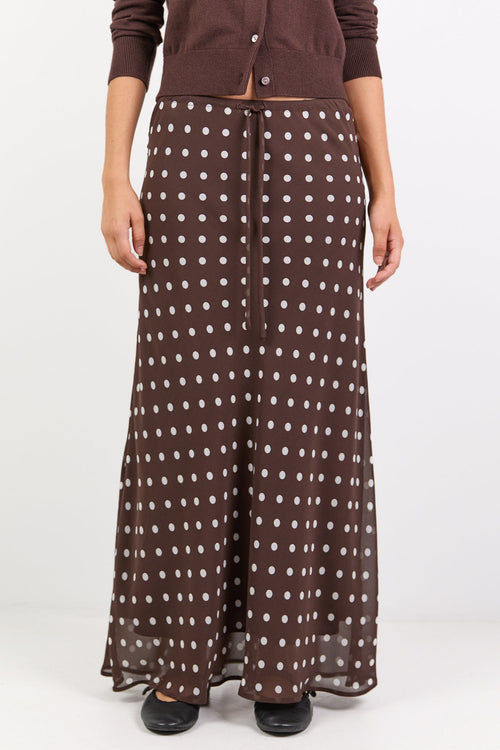 Woman wearing a brown cardigan and patterned skirt on a white background