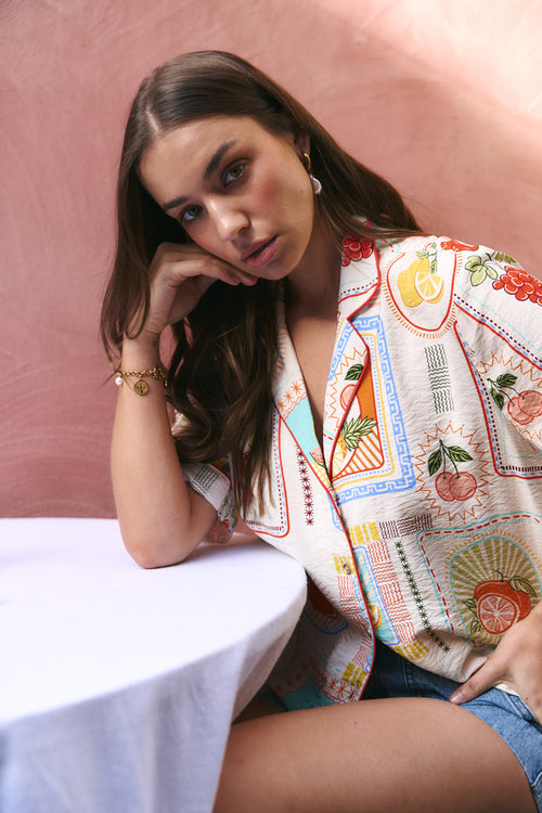 Woman wearing a colorful embroidered jacket against a pink background