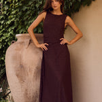 Woman in a dark dress standing against a textured wall with greenery