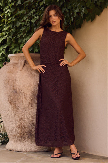 Woman in a dark dress standing against a textured wall with greenery