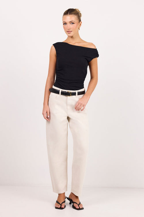 A woman modeling a black off-the-shoulder top and cream-colored wide-leg trousers with a black belt, standing against a plain white studio background.
