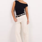 A woman modeling a black off-the-shoulder top and cream wide-leg jeans with a black belt, standing against a plain white studio background.