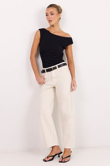 A woman modeling a black off-the-shoulder top and cream wide-leg jeans with a black belt, standing against a plain white studio background.