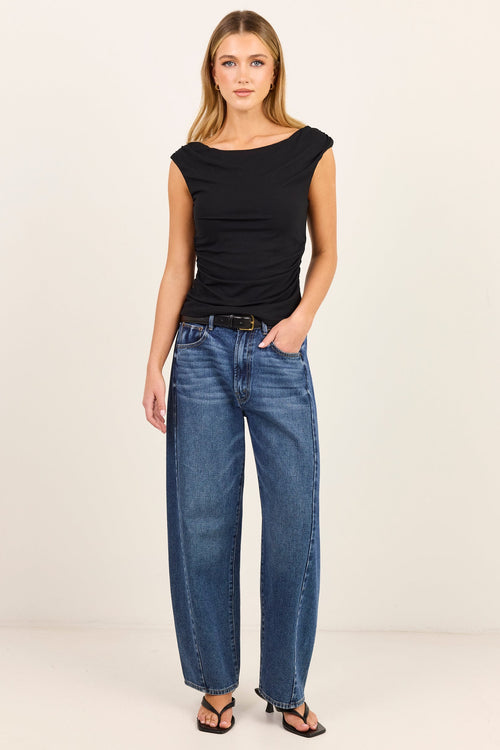 A woman modeling a black sleeveless top and wide-leg blue jeans with a black belt, standing against a plain off-white studio background.