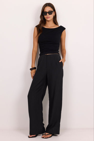 A woman modeling a black sleeveless top and matching black wide-leg pants against a plain white studio background.