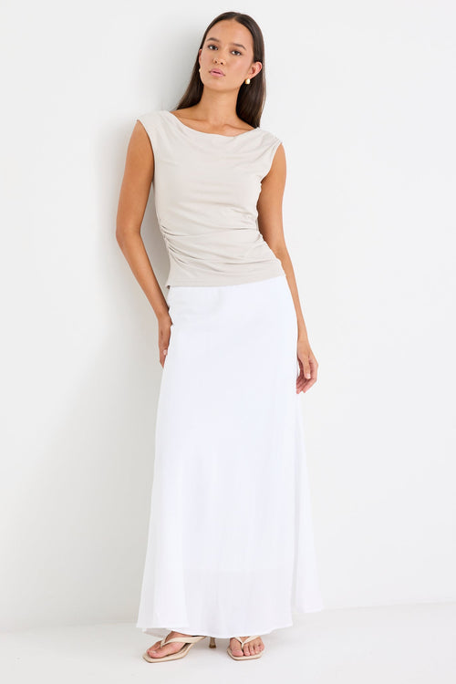 Woman wearing a stone-coloured sleeveless stretch top with a boat neckline, side ruching, and a fitted silhouette