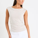 Woman wearing a stone-coloured sleeveless stretch top with a boat neckline, side ruching, and a fitted silhouette