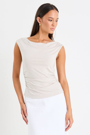 Woman wearing a stone-coloured sleeveless stretch top with a boat neckline, side ruching, and a fitted silhouette