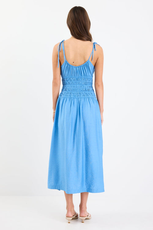 Woman wearing a bright blue strappy midi dress with tie-detail straps, shirred bodice, side split, and relaxed skirt.