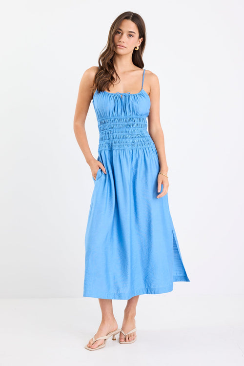 Woman wearing a bright blue strappy midi dress with tie-detail straps, shirred bodice, side split, and relaxed skirt.