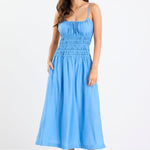 Woman wearing a bright blue strappy midi dress with tie-detail straps, shirred bodice, side split, and relaxed skirt.