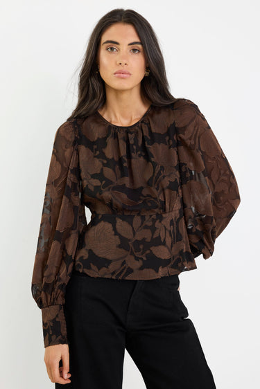 Woman wearing a brown floral blouse and black pants on a white background
