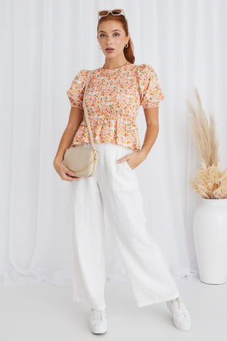 model in orange floral top and white pants and white sneakers