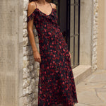 Woman in a floral dress standing against a stone wall.