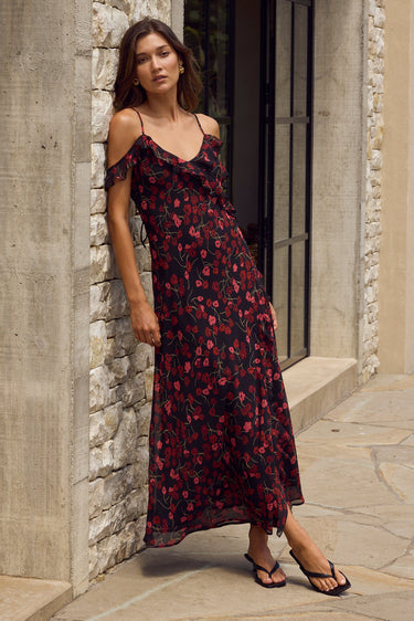 Woman in a floral dress standing against a stone wall.