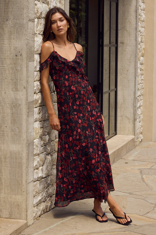 Woman in a floral dress standing against a stone wall.
