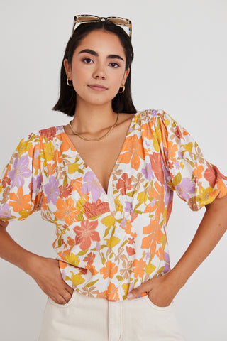 model wearing floral orange and yellow top and white shorts