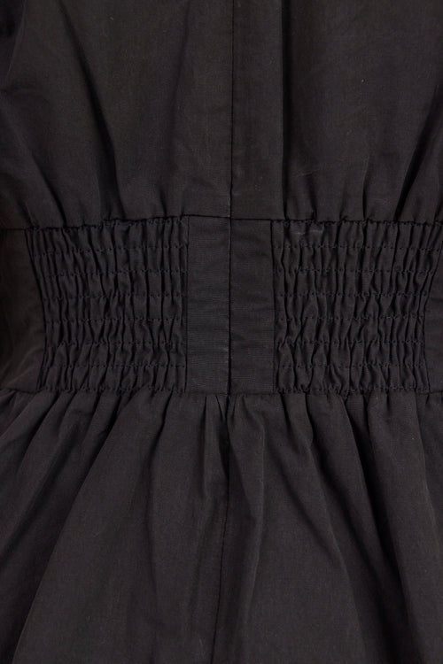 Close-up of a black dress showing the smocked waistband and gathered skirt fabric.