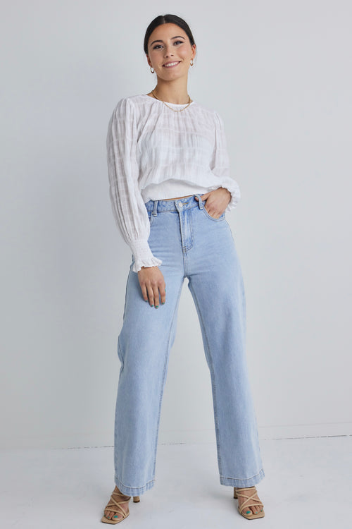 Model posing in white long sleeve cotton top and blue jeans