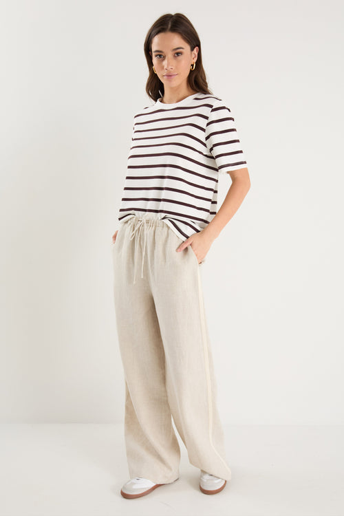 Woman in beige linen pants with side stripe detail and an elastic waistband, paired with a white stripe top. 