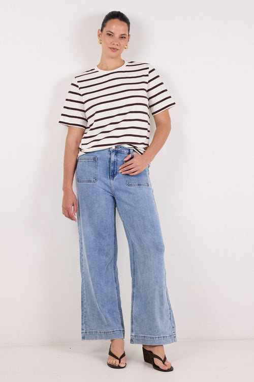 A model stands against a plain white studio background wearing a black and white horizontally striped short-sleeve t-shirt, light blue wide-leg denim jeans, and black sandals.